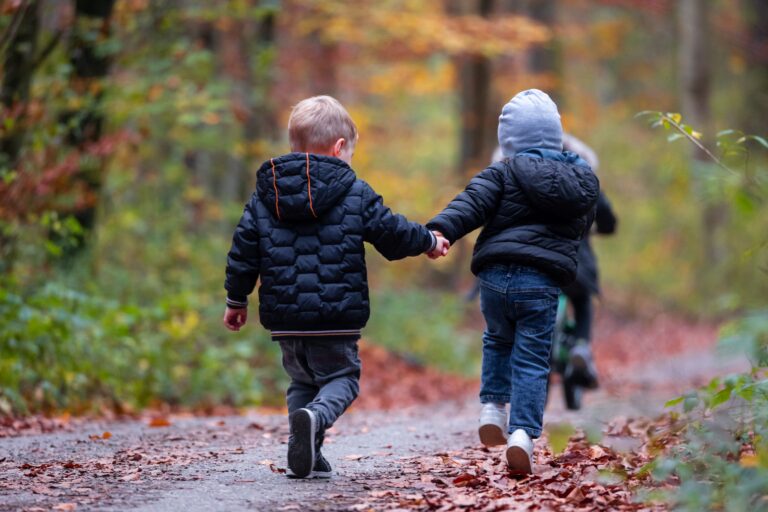 Two children walking down a woodland path, holding hands