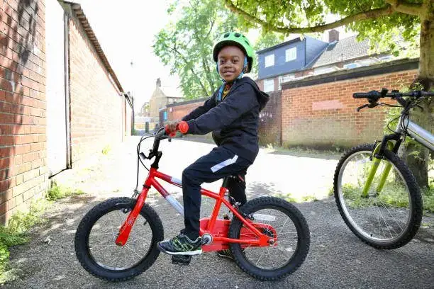 Young black boy wearing a green helmet on a red bike